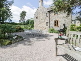An outdoor gravel patio with a large stone house in the background metal dining table and chairs a wooden bench with badminton rackets and shuttlecocks and a barbecue grill in view at Pentre Hall in Bronygarth near Chirk
