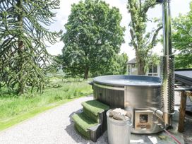 An outdoor hot tub with wood fire stove and steps surrounded by trees and grass at Pentre Hall in Bronygarth near Chirk