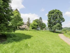 A grassy field with trees a gravel path and a stone building in the background at Pentre Hall in Bronygarth near Chirk