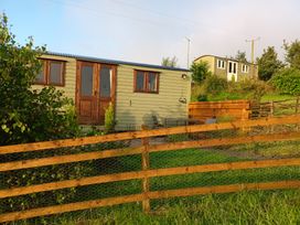 A shepherd's hut and wooden fence with greenery at The Herdsman Luxury Shepherds Hut in Barnoldswick