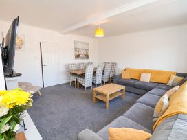 A living room with a gray sectional sofa with yellow accents a wooden coffee table a dining table with checkered chairs and a wall-mounted television at Banks View Filey in Filey