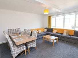 A living room with a wooden dining table and plaid chairs next to a large gray sectional sofa with yellow and beige cushions at Banks View Filey in Filey