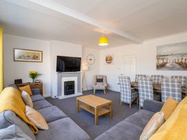 A living room with gray sofas yellow throws a wooden coffee table a wall mounted tv above a fireplace and a dining table with plaid chairs at Banks View Filey in Filey