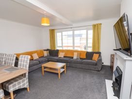 A living room with a large gray sectional sofa with orange and beige cushions a wooden coffee table plaid dining chairs and a wall mounted television above a fireplace at Banks View Filey in Filey