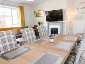 A dining table with placemats and a small plant with upholstered chairs in a living room with a sofa yellow curtains a wall-mounted television and a floor lamp at Banks View Filey in Filey