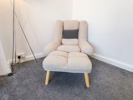 A beige upholstered armchair with a dark gray cushion and a floor lamp in a corner on a gray carpeted floor at Banks View Filey in Filey