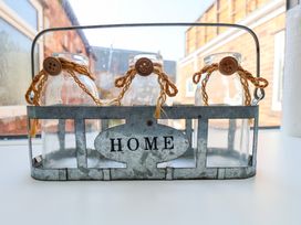 Three glass jars with rope and button decorations in a metal holder labeled home on a windowsill
