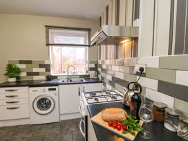 A kitchen with a washing machine a stove and a counter with bread tomatoes and a wine bottle at Banks View Filey