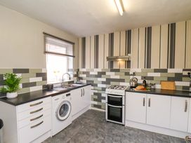 A kitchen with white cabinets a washing machine black countertops and a gas stove at Banks View Filey in Filey