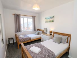 A bedroom with two single beds, a chest of drawers with a lamp and mirror, a window with curtains, and a wall painting at Banks View Filey in Filey