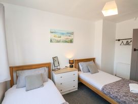A bedroom with two single beds a bedside table with a lamp and a mirror a wall painting and hangers on a rod at Banks View Filey in Filey