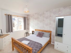A bedroom with a wooden bed, bedside table with lamp, white wardrobe with mirror, chest of drawers, and grey curtains at Banks View Filey