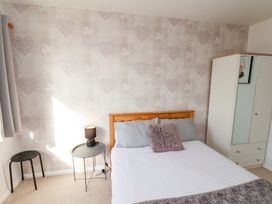 A bedroom with a wooden bed, a white wardrobe, a round side table with a lamp, and a patterned wallpaper at Banks View Filey in Filey