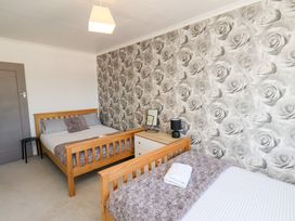 A bedroom with two wooden beds a nightstand with a lamp and picture frame and a floral patterned wall at Banks View Filey