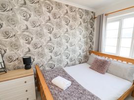 A bedroom with a wooden bed frame white and purple bedding a dresser a black lamp and floral wallpaper at Banks View Filey in Filey