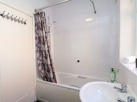 A bathroom with a bathtub shower combination white tiles a sink with faucets a patterned shower curtain and a towel on the windowsill at Banks View Filey in Filey