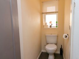 A small bathroom with a white toilet a window with a blind three toilet paper rolls a flower decoration and a cleaning spray on the window sill at Banks View Filey in Filey