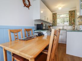 A kitchen with a wooden dining table and chairs a microwave and a window with patterned curtains at 8 The Park in Kilkhampton