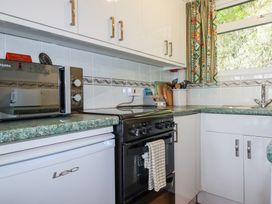 A kitchen with a black oven, white cabinets, a microwave, utensils in a container, and a window with patterned curtains at 8 The Park in Kilkhampton