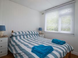 A bedroom with a bed with striped bedding blue towels on the bed and two bedside tables with lamps at 8 The Park in Kilkhampton