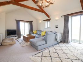 A living room with a gray sectional sofa with yellow pillows wooden coffee table and a television on a stand at Penpethy Farm in Tintagel