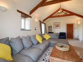 A living room with a grey sectional sofa with yellow cushions a wooden coffee table under wooden ceiling beams at Penpethy Farm in Tintagel