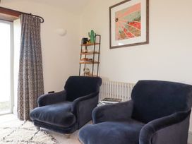 Two dark armchairs near a window with patterned curtains a small shelf with decorative items and a framed picture on the wall at Penpethy Farm in Tintagel