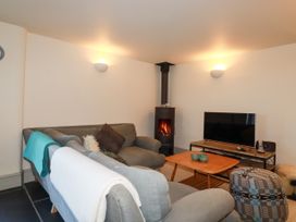A living room with gray sofas a wood stove a wooden coffee table a television on a stand and a patterned ottoman at Penpethy Farm in Tintagel