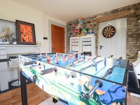A game room with a foosball table a dartboard on the door shelves with board games and a mounted owl at Penpethy Farm in Tintagel