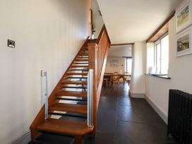 A hallway with wooden stairs leading up and a dining table with chairs in the background at Penpethy Farm in Tintagel