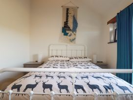 A bedroom with a white metal bed frame with deer print bedding and a wall hanging above at Penpethy Farm in Tintagel