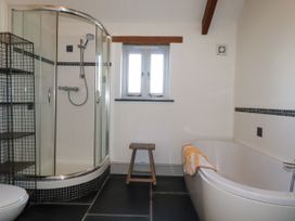 A bathroom with a shower enclosure a bathtub a wooden stool and a metal shelving unit at Penpethy Farm in Tintagel
