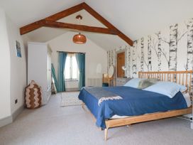A bedroom with a wooden bed with blue bedding a wardrobe a full length mirror a dressing table and wallpaper with tree designs at Penpethy Farm in Tintagel