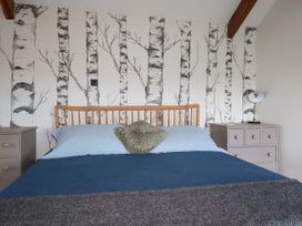 A bedroom with a wooden bed frame blue bedding two gray bedside tables and wallpaper with birch tree designs at Penpethy Farm in Tintagel