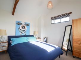A bedroom with a blue bedspread and two bedside tables with lamps a cow painting above the bed a window with a patterned curtain a standing mirror and a wooden wardrobe at Penpethy Farm in Tintagel