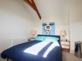 A bedroom with a bed featuring blue bedding and pillows two bedside tables with lamps a cow painting on the wall and wooden ceiling beams at Penpethy Farm in Tintagel