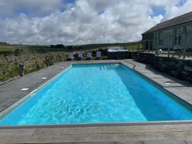 An outdoor swimming pool with lounge chairs and a hot tub near a building at Penpethy Farm in Tintagel