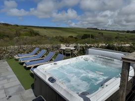 An outdoor area with a hot tub surrounded by four lounge chairs and a round wooden table with chairs overlooking fields at Penpethy Farm in Tintagel