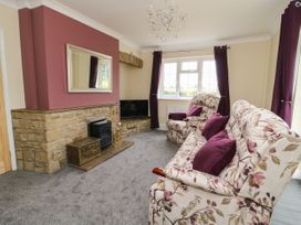 A living room with patterned sofas and purple cushions near a stone fireplace with a mirror above at 2 Crosslands in Stockton-On-The-Forest