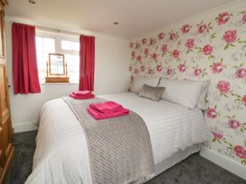 A bedroom with a bed with white bedding and pink towels near a window with red curtains at 2 Crosslands in Stockton-On-The-Forest