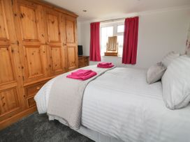 A bedroom with a large wooden wardrobe white bed with pink towels and red curtains at 2 Crosslands in Stockton-On-The-Forest