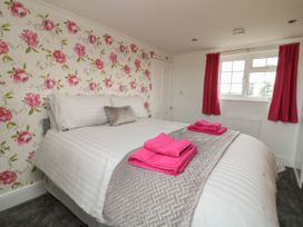 A bedroom with a double bed with white striped bedding and pink towels on a gray bed runner with floral wallpaper and pink curtains at 2 Crosslands in Stockton-On-The-Forest