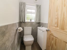 A small bathroom with a toilet a sink unit a window with curtains and a wooden door at 2 Crosslands in Stockton-On-The-Forest