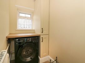 A laundry room with a black washing machine below a wooden countertop and cream cabinets by a small window at 2 Crosslands in Stockton-On-The-Forest