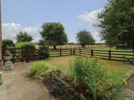 A fenced backyard garden with grass, flower beds, and trees at 2 Crosslands in Stockton-On-The-Forest