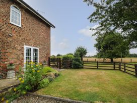 An outdoor garden area with grass flowers shrubs a brick house with white framed double doors and windows and wooden fences at 2 Crosslands Stockton-On-The-Forest