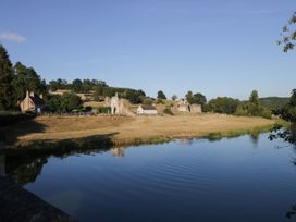 A river with grassy banks and old stone buildings in the background at 2 Crosslands in Stockton-On-The-Forest
