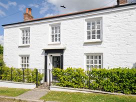 The front exterior of a white stone house with a black door white window shutters and a garden with shrubs behind a black metal fence at Quay House in Charlestown