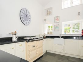 A kitchen with white cabinets black countertops a beige oven a farmhouse sink two windows and a large wall clock at Quay House in Charlestown