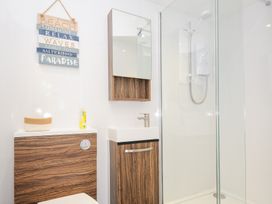 A bathroom with a wall-mounted mirror cabinet a sink a wooden cabinet a glass shower enclosure and a decorative wall sign at Quay House in Charlestown